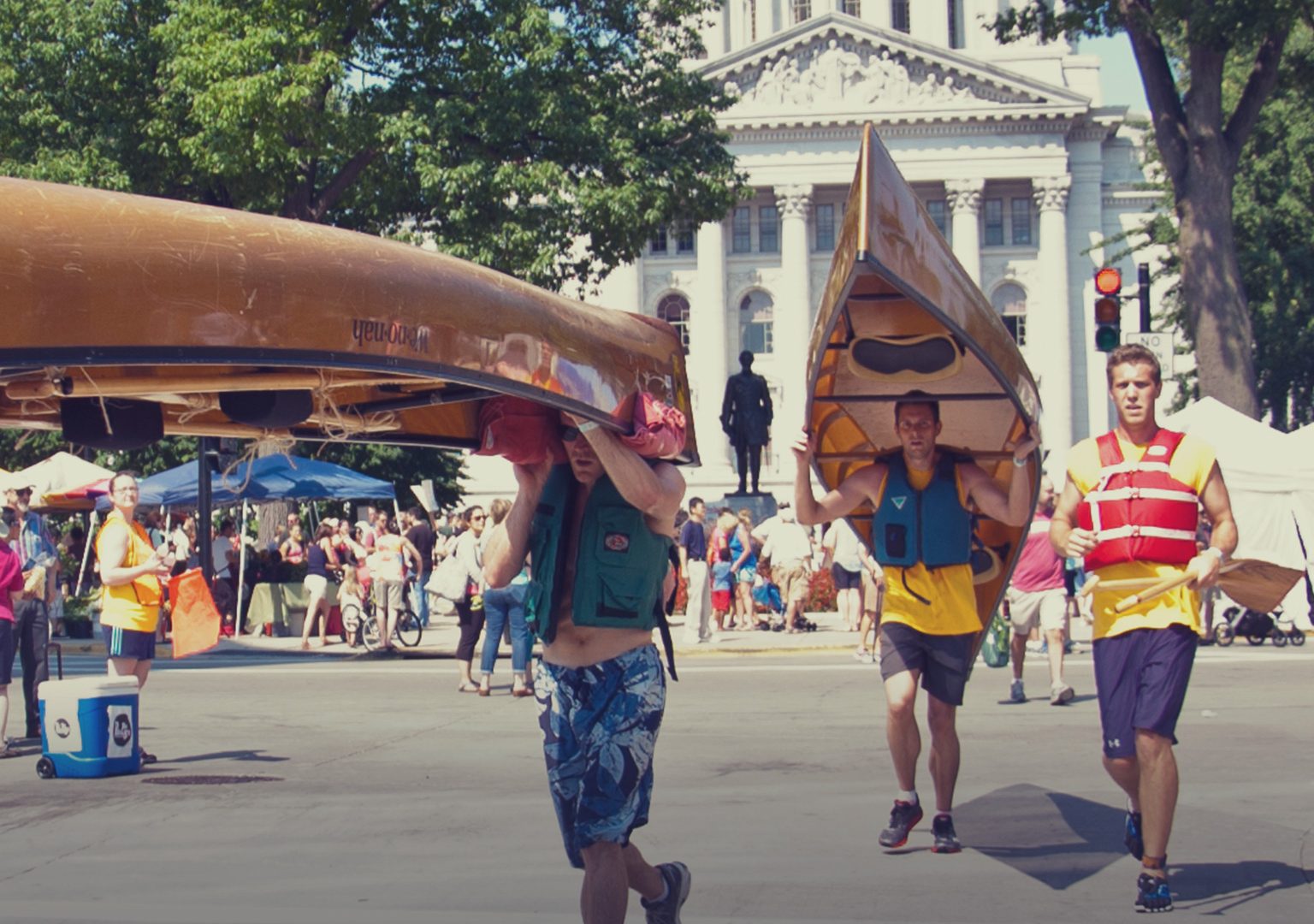 Race participants carrying canoes over their heads running across street with Capitol building in background